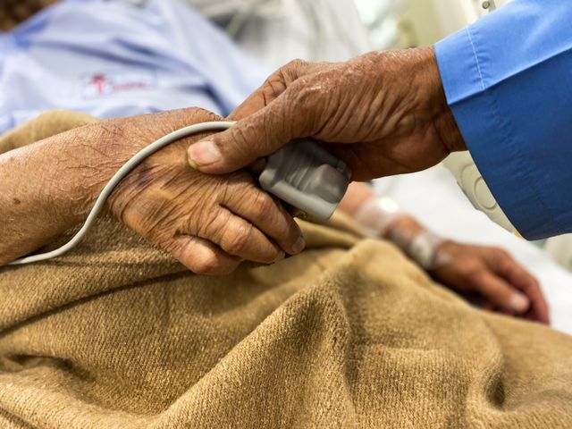 Elderly hospital patient being comforted by someone holding her hand